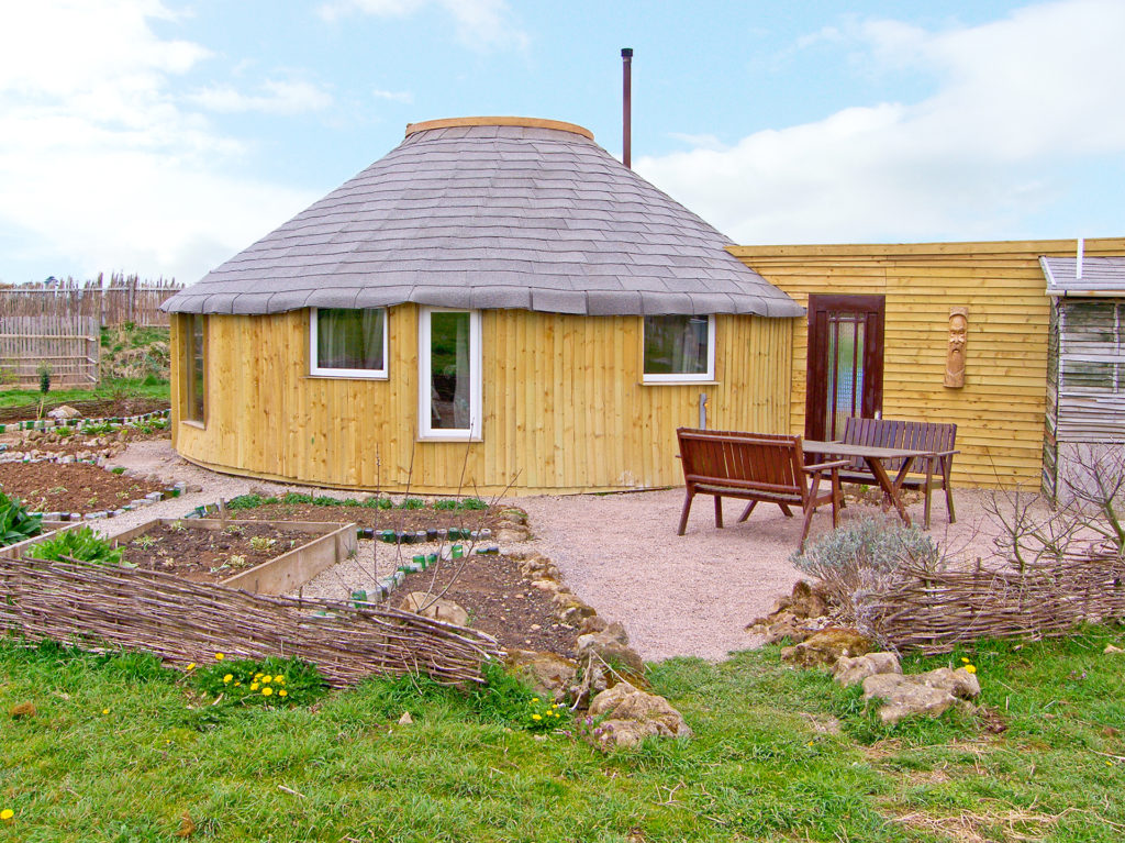 Circular wooden clad hut with vegetable beds and outdoor seating area