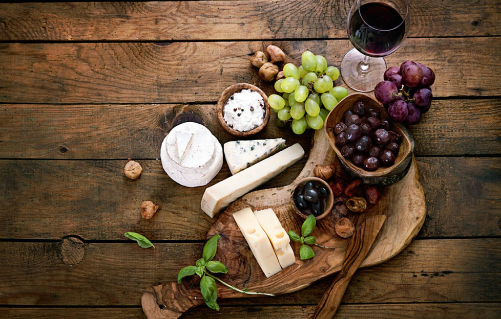 Artistic arrangement of cheeses, grapes, dried fruit, red wine and beautiful curved dark wooden board