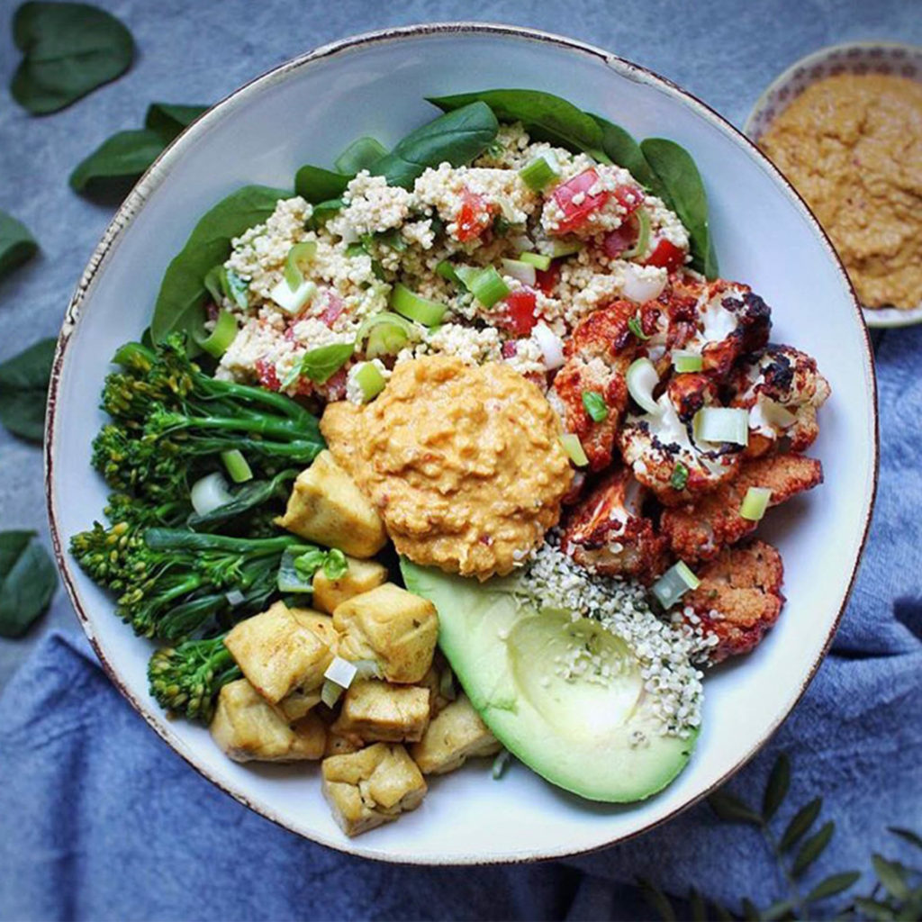 Plate of delicious veg - roasted broccoli, spiced cauliflower, roast potatoes, grain salad and a big dollop of hummus in the middle