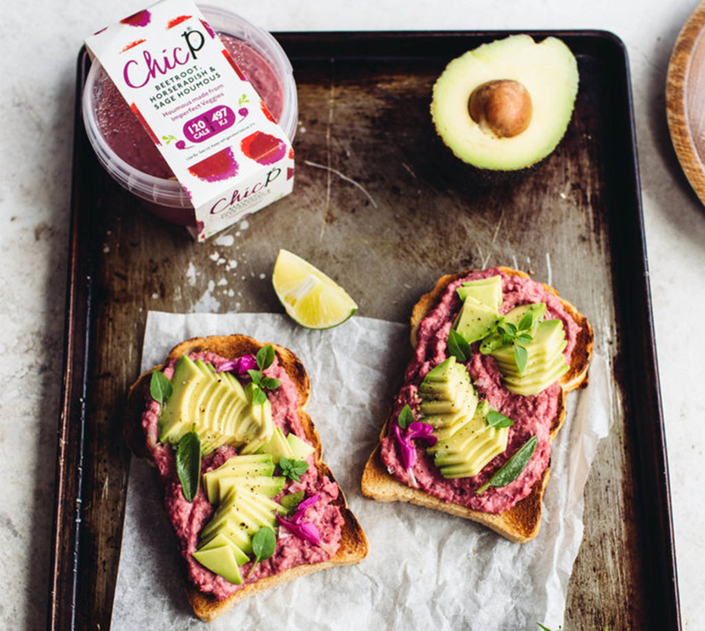 Baking tray with tub of Chic P beetroot hummus, half an avocado and 2 slices of toast spread with the hummu, avocado slices on top