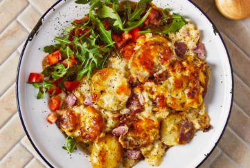 Plate of golden cheesy topped potato and bacon gratin bake with rocket salad