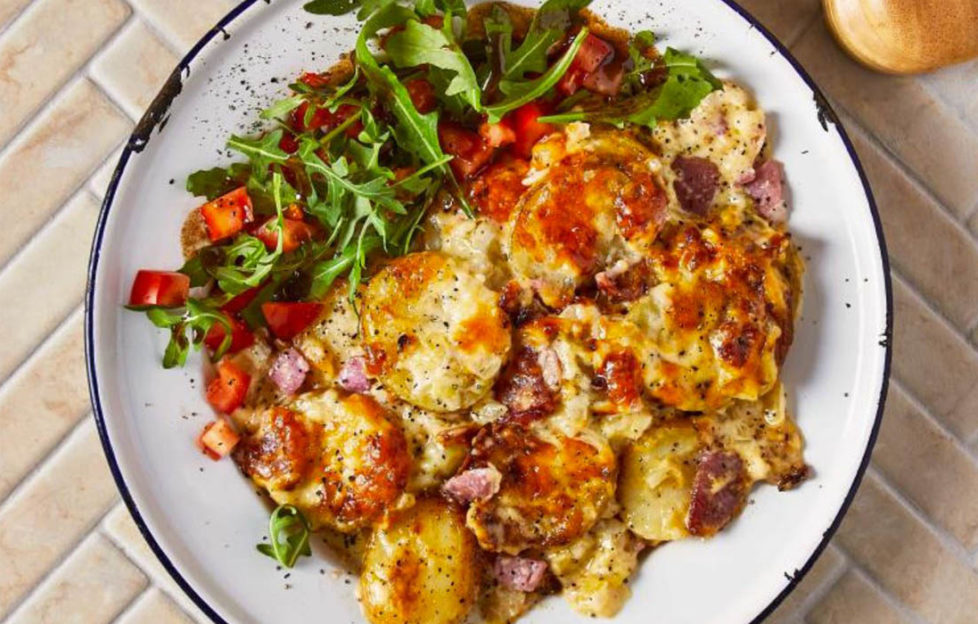 Plate of golden cheesy topped potato and bacon gratin bake with rocket salad