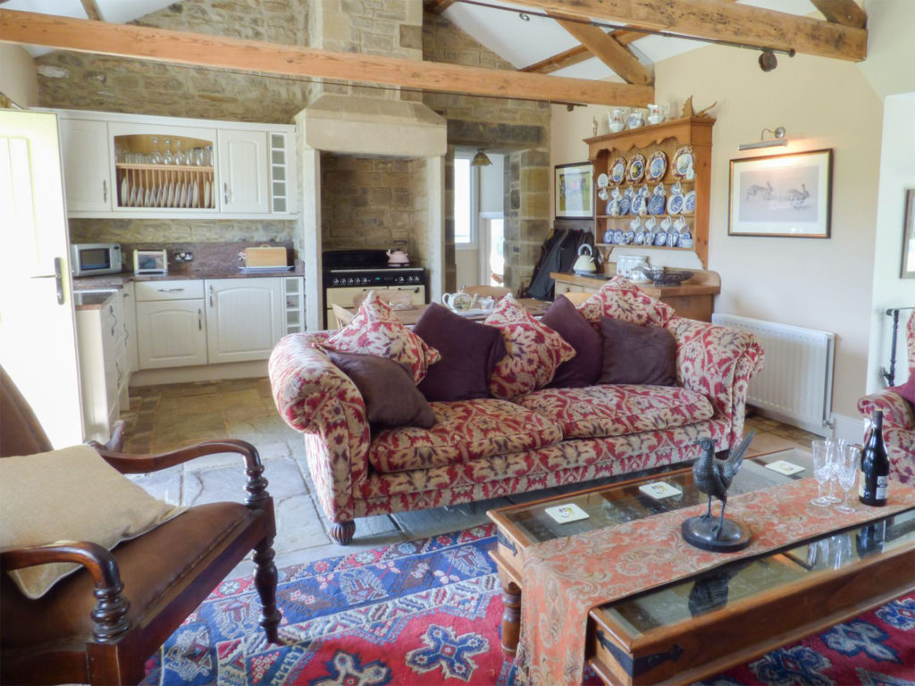 Cottage living room with chintz sofa and dresser with plates, kitchen behind