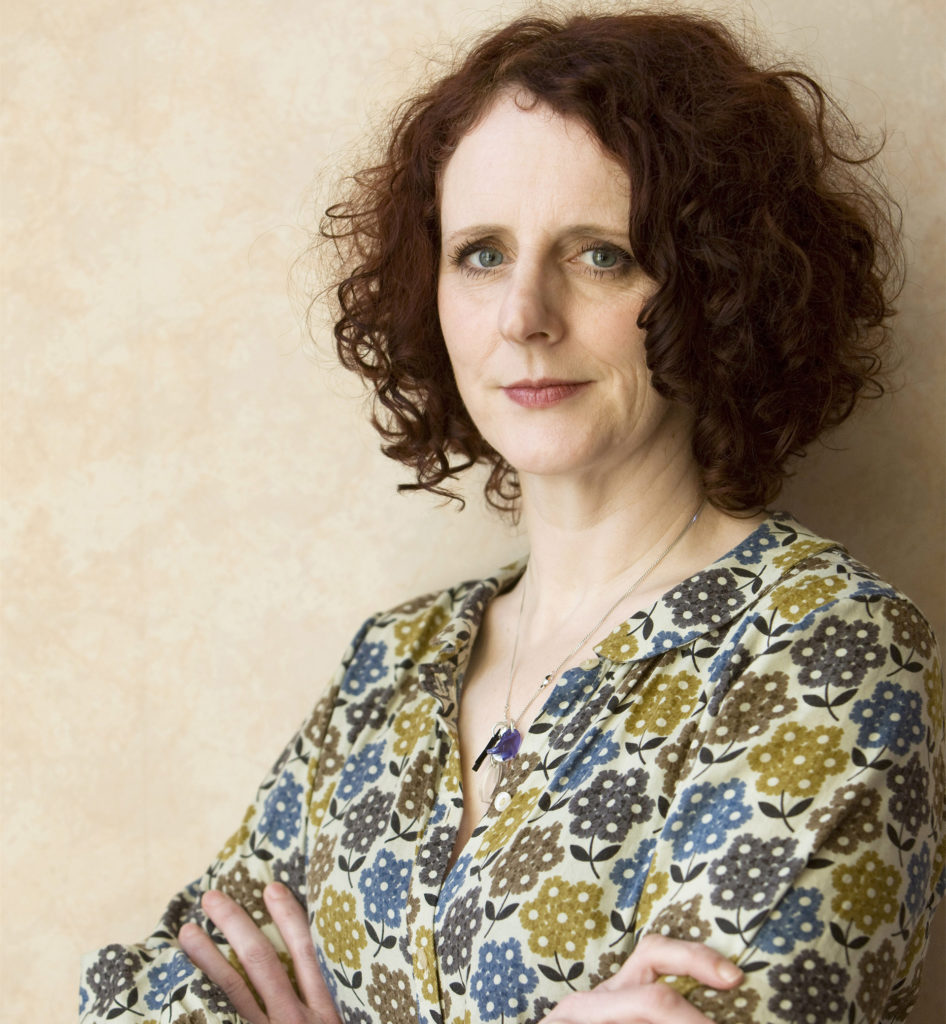 Portrait of author Maggie O'Farrell, jaw length dark curly hair, serious expression, arms folded