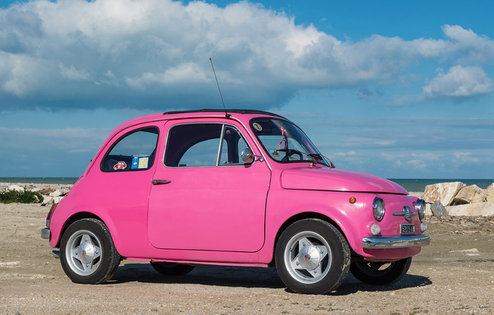 Bright pink small car, Fiat 500, parked by the sea on a sunny day