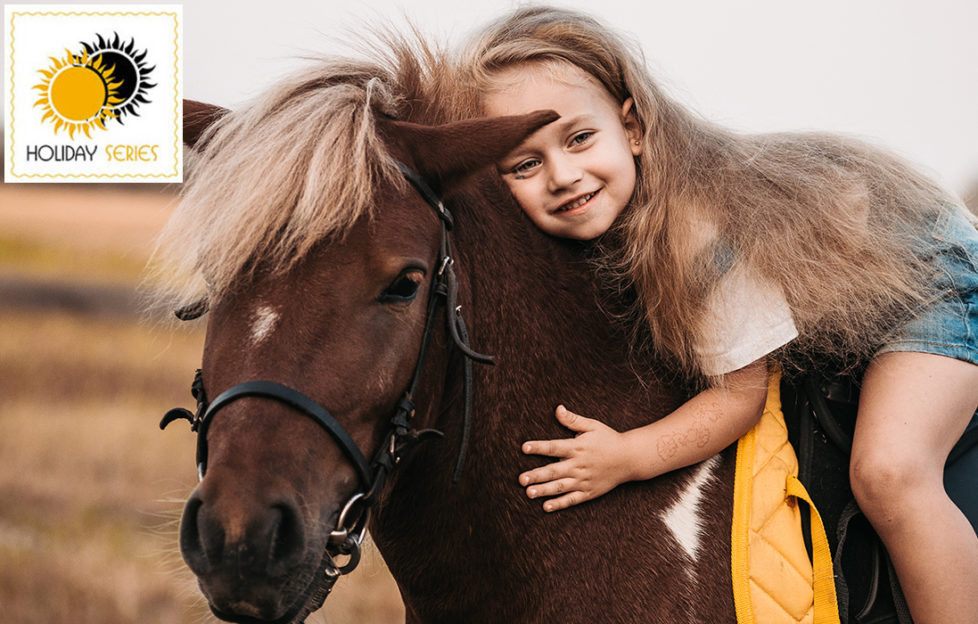 Girl on Shetland pony's back, leaning forward to hug it