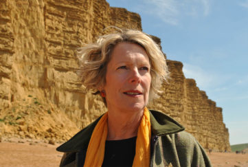 Author Rosanna Ley, blonde middle aged woman in rich yellow scarf and green walking jacket standing by yellow cliffs