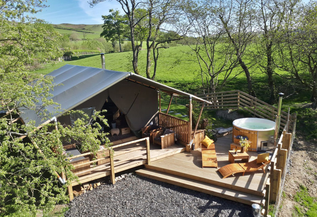 Tarpaulin roofed holiday chalet with loungers and hot tub on deck, countryside behind