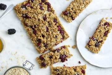 Slab of fruity flapjack traybake, 4 pieces cut, fresh blackberries and jar of oats on the side