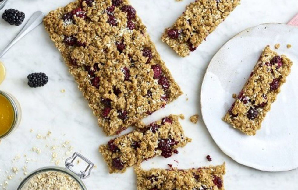 Slab of fruity flapjack traybake, 4 pieces cut, fresh blackberries and jar of oats on the side