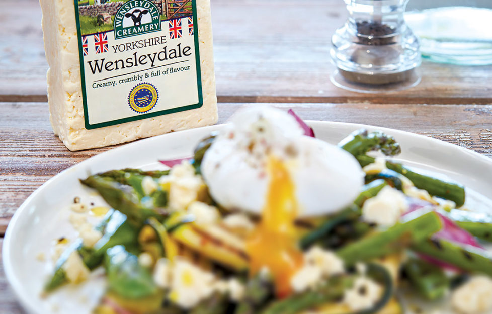 Plate of vegetables with crumbled cheese, poached egg and pack of Wensleydale cheese behind