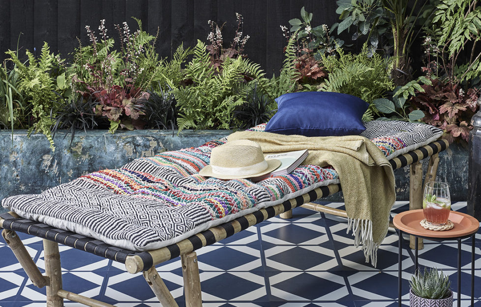 Bamboo garden bed on tiled blue and white patio, narrow bed of ferns against dark stained fence