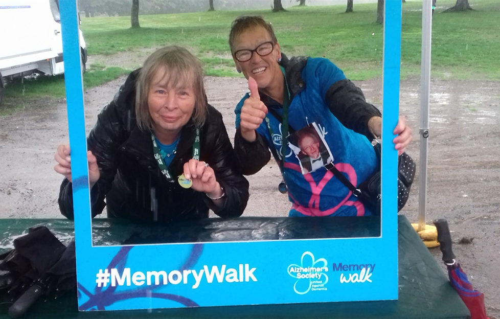 Two women show off their medals posing in a cardboard frame for Alzheimers Memory Walk, cold wet day