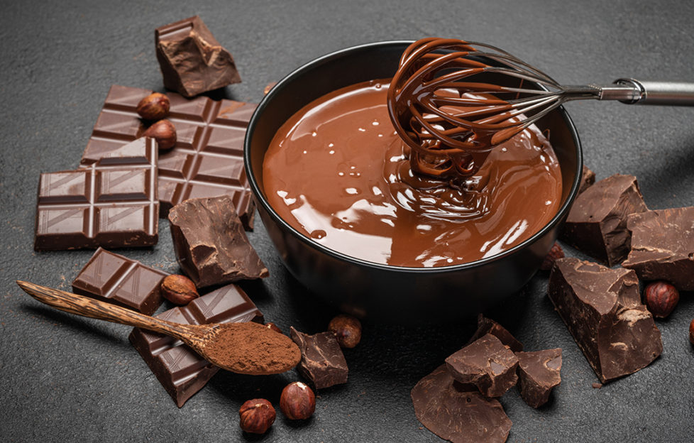 Bowl of melted chocolate and whisk, chocolate pieces and hazelnuts scattered around