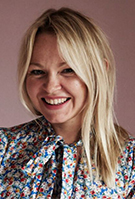 Head and shoulders of Rosie Birkett, young, blonde, laughing, wearing floral blouse with pussycat bow