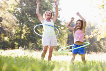 Grandmother and granddaughter at a park hula hooping and smiling;