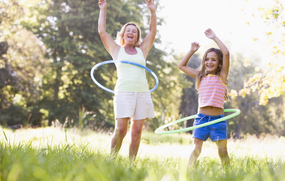 Grandmother and granddaughter at a park hula hooping and smiling;