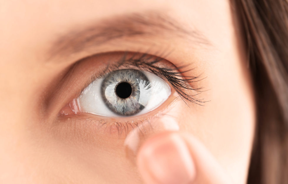 Close up view of young woman putting contact lens in her eye;