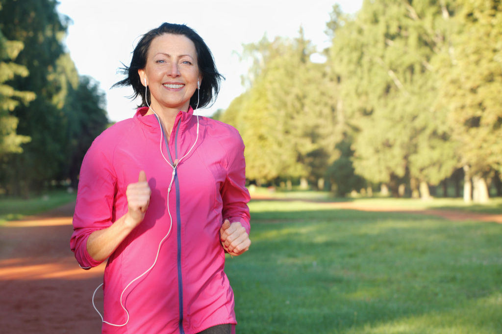 Portrait of elderly woman running with headphones in the park in early morning. Attractive looking mature woman keeping fit and healthy.;
