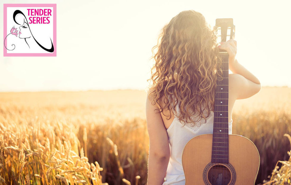 Girl looks out over golden cornfield, guitar over her shoulder