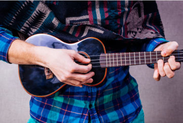 Person in bright checked shirt and ethnic scarf playing ukelele