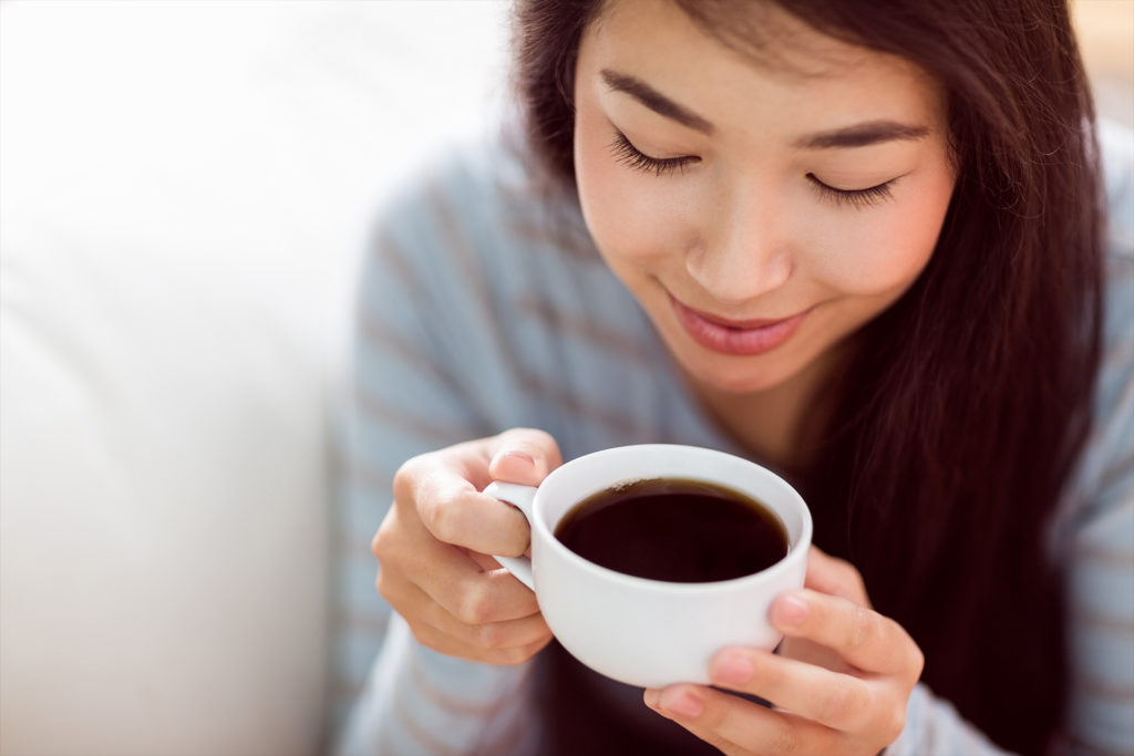Asian woman relaxing on couch with coffee at home in the living room