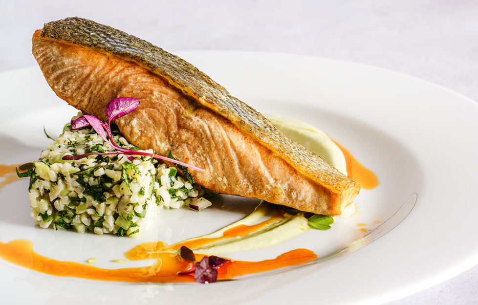 Fillet of trout on plate balanced on "block" of tabbouleh, grains and herbs, orange saffron sauce drizzled around