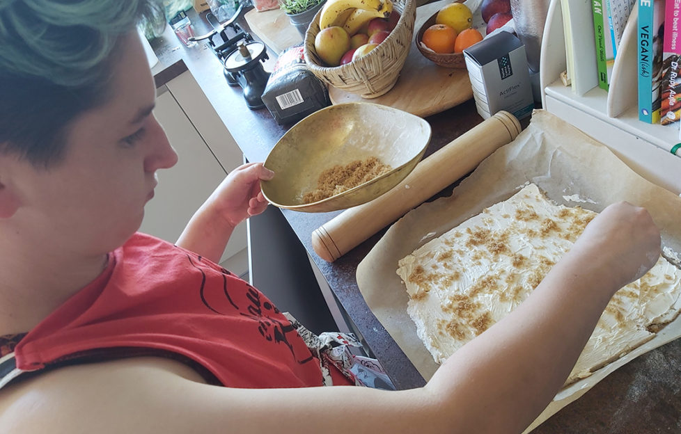 Young woman in red apron sprinkles sugar on a rectangle of pastry, easy baking