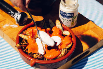 Terracotta dish of golden potatoes with rich tomato sauce and garlic mayonnaise, jar of Hellmanns Vegan Mayonnaise, sunny day outdoors