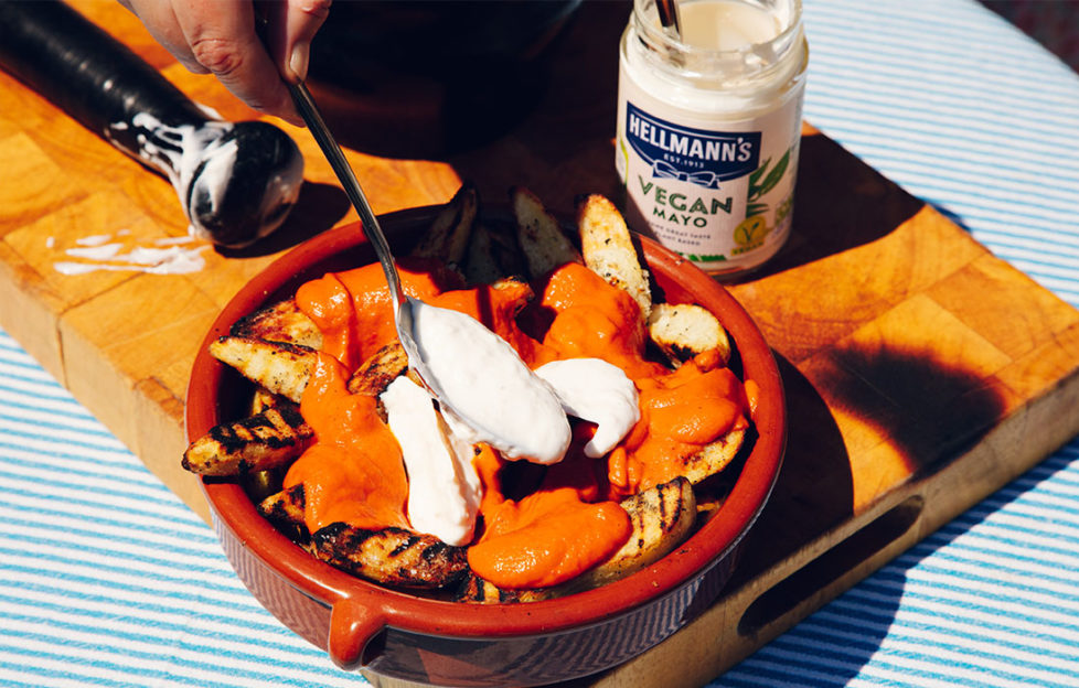 Terracotta dish of golden potatoes with rich tomato sauce and garlic mayonnaise, jar of Hellmanns Vegan Mayonnaise, sunny day outdoors