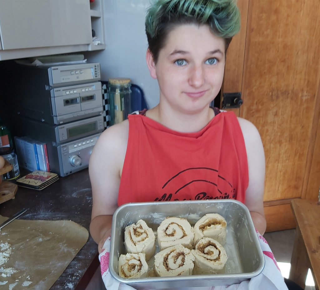 Young woman holding baking tin containing 6 rolled slices of filled pastry