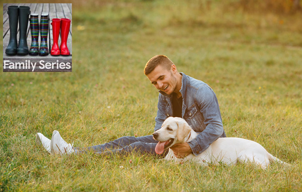 Happy young man sits on grass hugging golden labrador