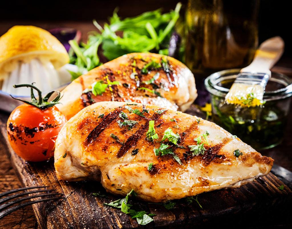 Marinated grilled healthy chicken breasts cooked on a summer BBQ and served with fresh herbs and lemon juice on a wooden board, close up view; 