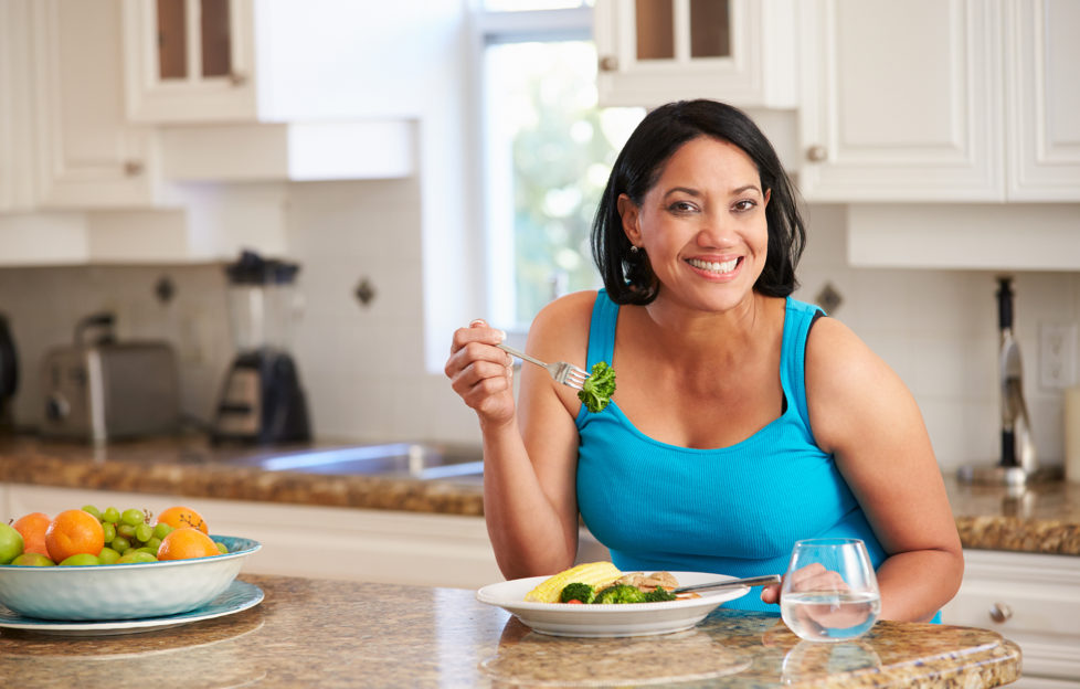 Overweight Woman Eating Healthy Meal in Kitchen;