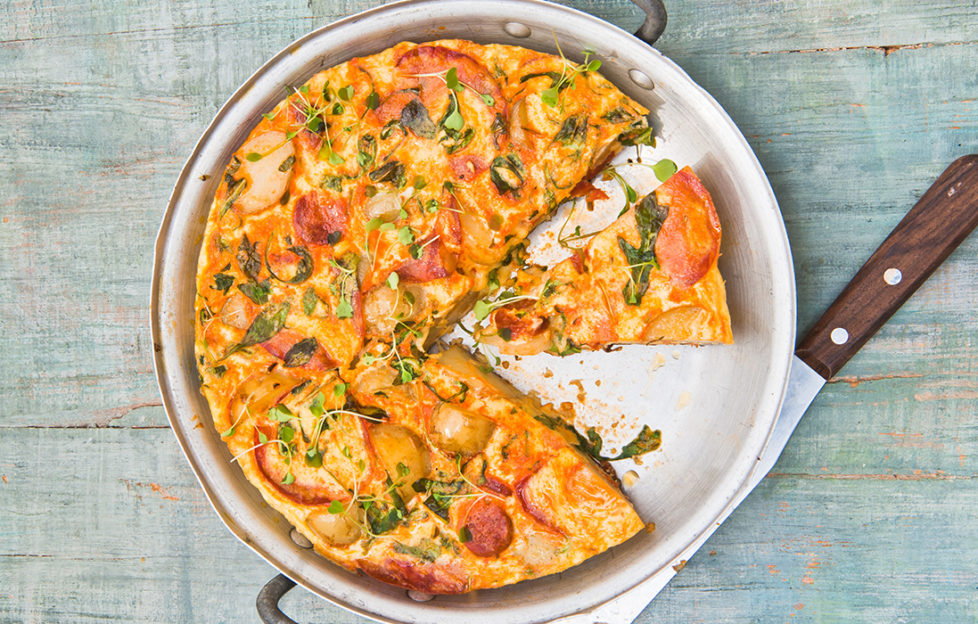 Golden tortilla with sausage pieces, sprinkled with herbs