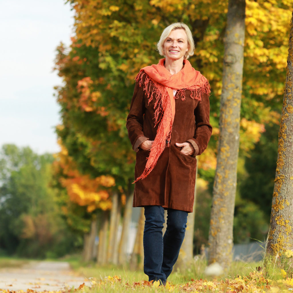 Happy mature woman in front of golden autumn leaves enjoys leisure time