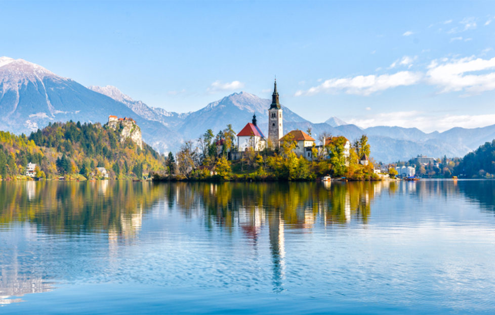 Lake Bled, fairytale towers and steep roofs on wooded island reflected in clear lake