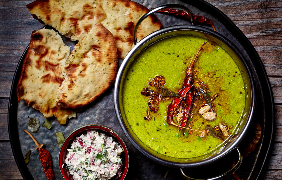 Bowl of beauriful pea green dip garnished with dried chilli and other spices, pot of white coconut chutney and golden toasted naan bread