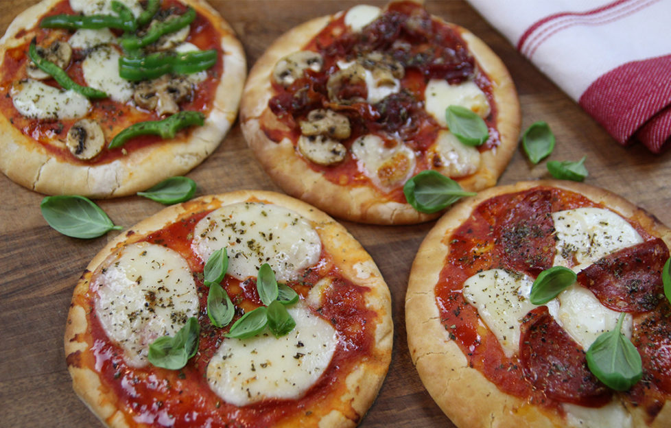 4 mini pizzas topped with tomato sauce, mozzarella slices, fresh basil and parma ham