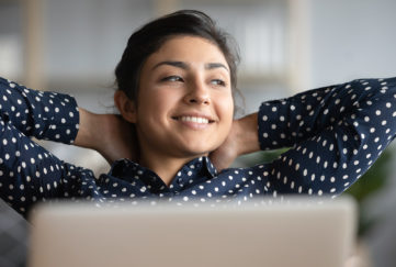 Happy satisfied indian woman rest at home office sit with laptop hold hands behind head, dreamy young lady relax finished work feel peace of mind look away dream think of future success concept;