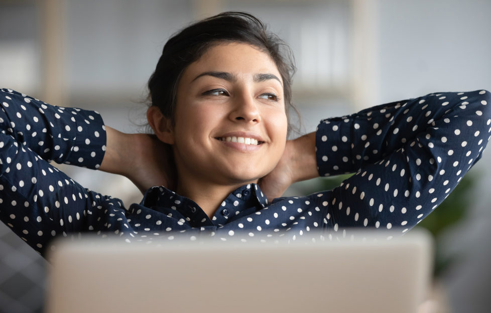 Happy satisfied indian woman rest at home office sit with laptop hold hands behind head, dreamy young lady relax finished work feel peace of mind look away dream think of future success concept;