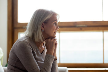 Side view of sad thoughtful middle-aged mature woman sit on couch at home look in window distance mourning, upset pensive senior female lost in thoughts thinking or pondering over past;