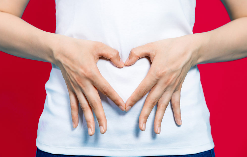 young woman who makes a heart shape by hands on her stomach.;