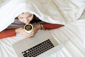 Woman working on laptop under the duvet