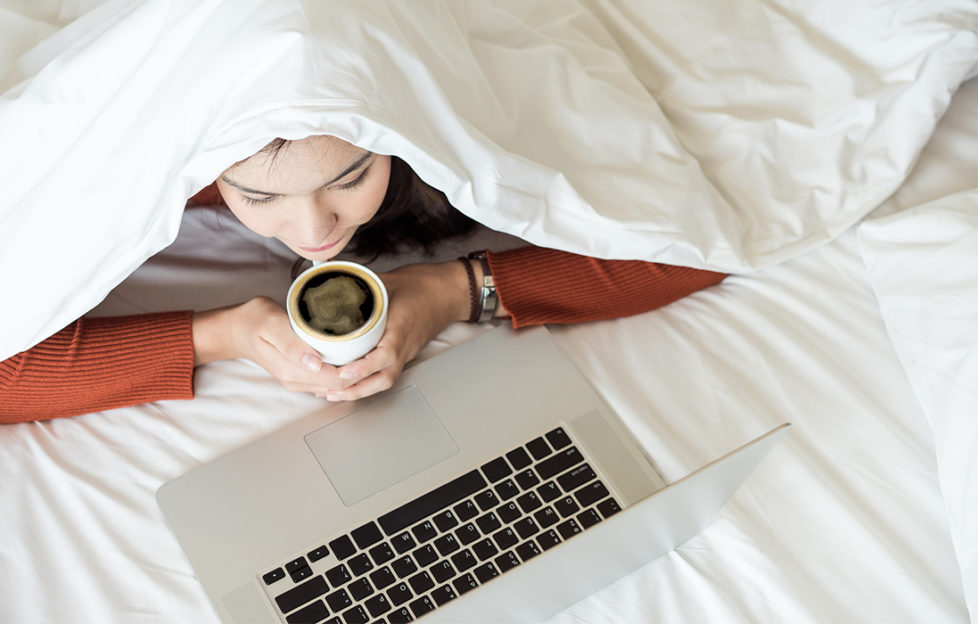 Woman working on laptop under the duvet