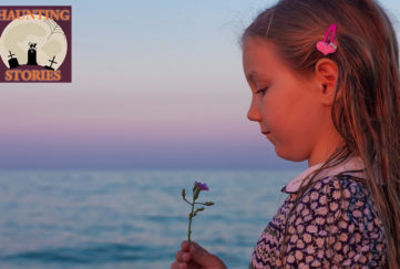 Girl aged around 8 stands by sea at dusk, looking at wild flower, she has long hair and a traditional summer dress with floral print and white collar
