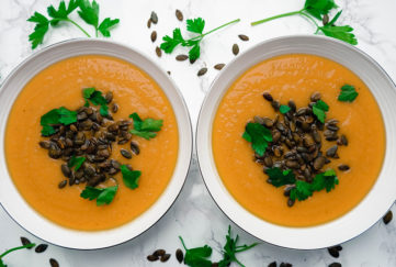 2 bowls of orange soup topped with toasted seeds, flat leaf parsley sprinkled around
