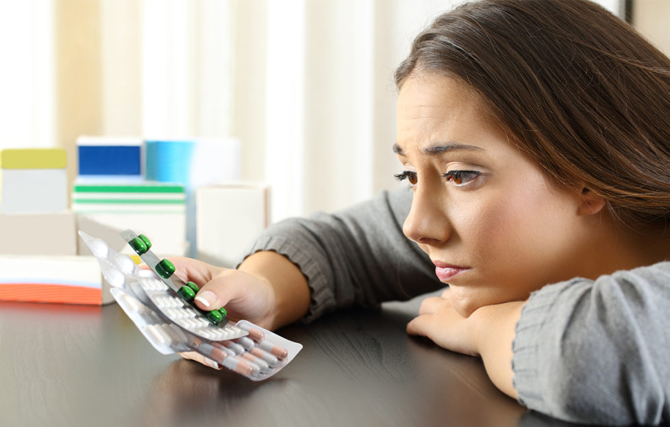 Woman stares glumly at a handful of pill sheets