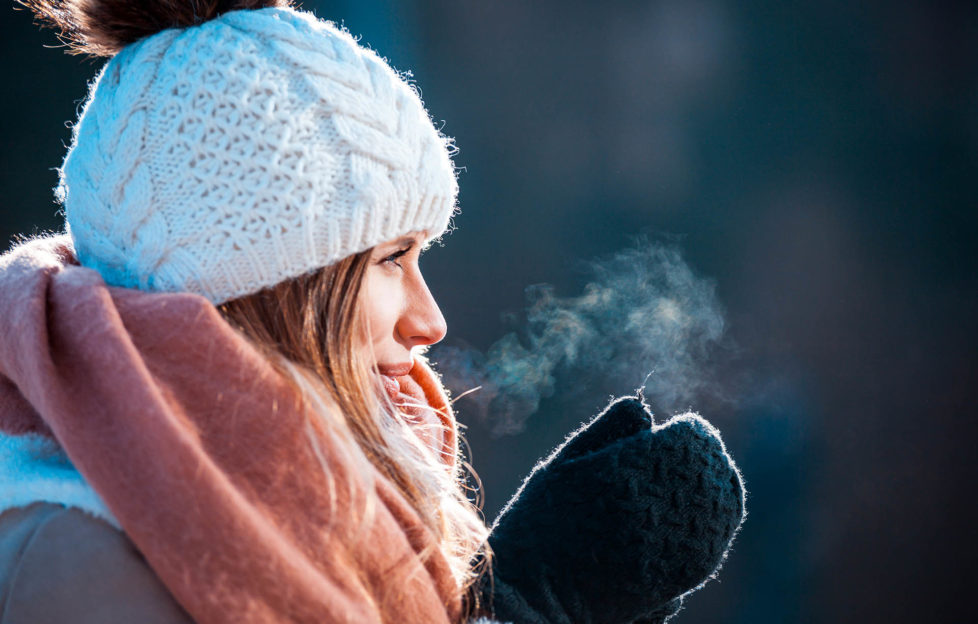 Woman breathing on her hands to keep them warm at cold winter day;