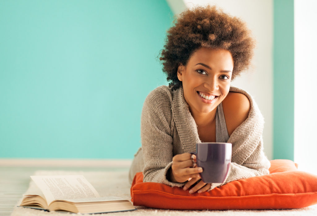 Beautiful young African woman enjoying a cup of coffee while relaxing at home.; 